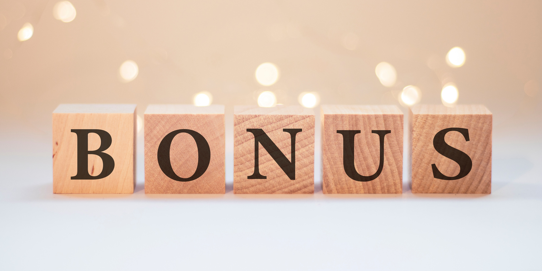 Word bonus cube wood on wooden table white background. Concept bonus is any financial compensation.